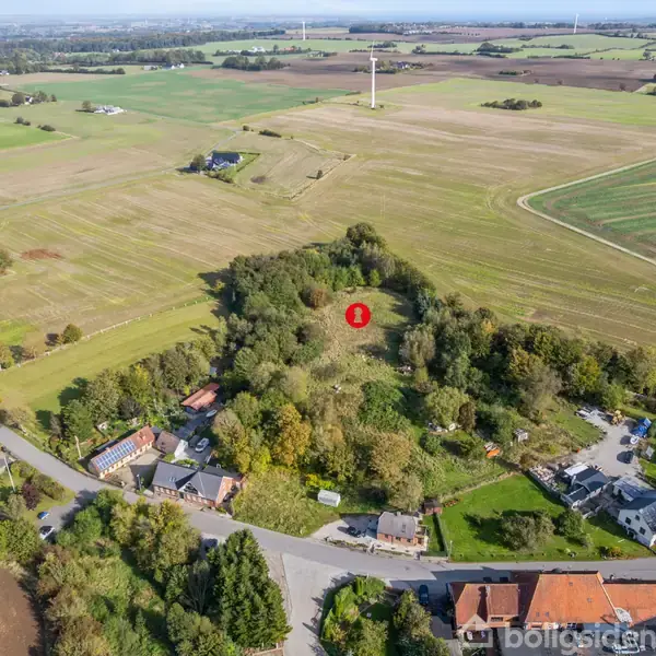 Et landligt område med spredte huse i forgrunden omgivet af marker og grønne træer. En rød markering med tallet "1" vises midt i et skovområde.