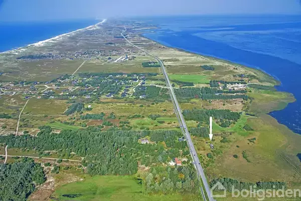 Landskab set fra luften med en lang vej, der strækker sig gennem åbne grønne områder og landsbyer, omgivet af kystlinjen og havet til venstre og højre.