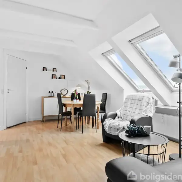 En moderne stue har en sort sofa nær vinduer med udsigt. Et spisebord med stole står i hjørnet, omgivet af minimalistisk dekoration. En vægklokke viser tidspunktet.