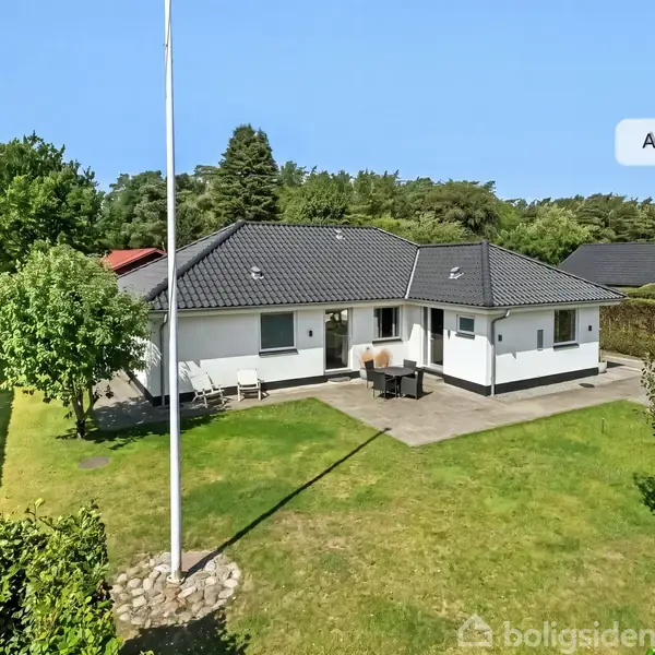 Hvid bungalow står i en solrig have med græsplæne og flagstang. Terrasse med bord og stole. Omgivet af hæk og træer. Tekst: "AI visualisering".