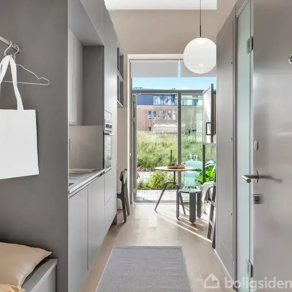 En smal entré leder ud til en lys altan med udsigt over en have. Venstre væg har en hængekrog med en hvid taske.