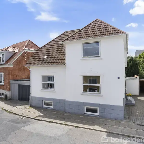 En hvid to-etagers bolig med brun tegltag står langs en række af huse. Forhaver er flisebelagt, og en garagevogn ses længere ned ad vejen. En blå himmel udgør baggrunden.