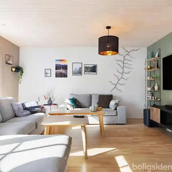 Stue med grå sofaer og træbord, hænger en sort lampe fra loftet. Væggen har billeder og klatrende planteudsmykning. Der er et stort TV på en grøn væg, og lys strømmer ind fra vinduerne.