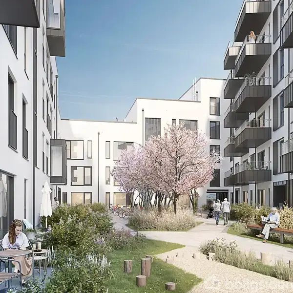 En gårdhave med moderne lejlighedsbygninger og altaner. Personer sidder ved borde, nogle går eller cykler på en sti forbi blomstrende træer og planter under en blå himmel.