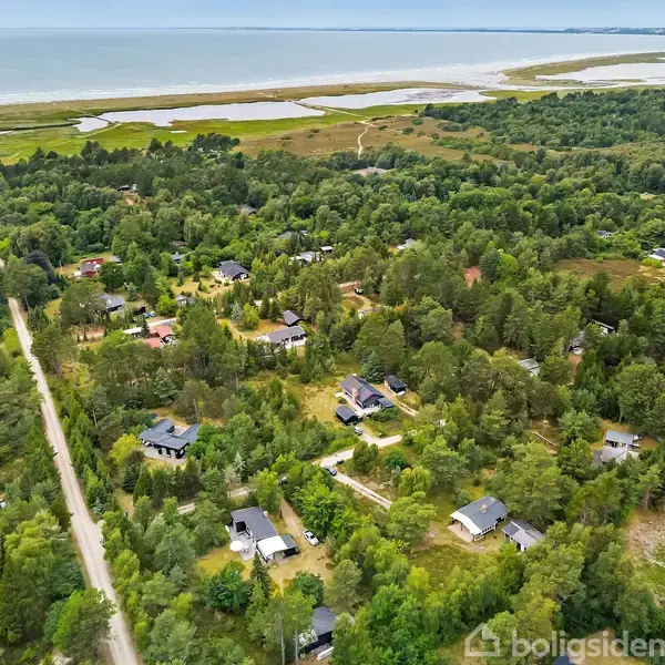 En række huse ligger spredt i en skovklædt region nær kysten, med en vej, der skærer gennem landskabet. I baggrunden ses kystlinjen og havet.