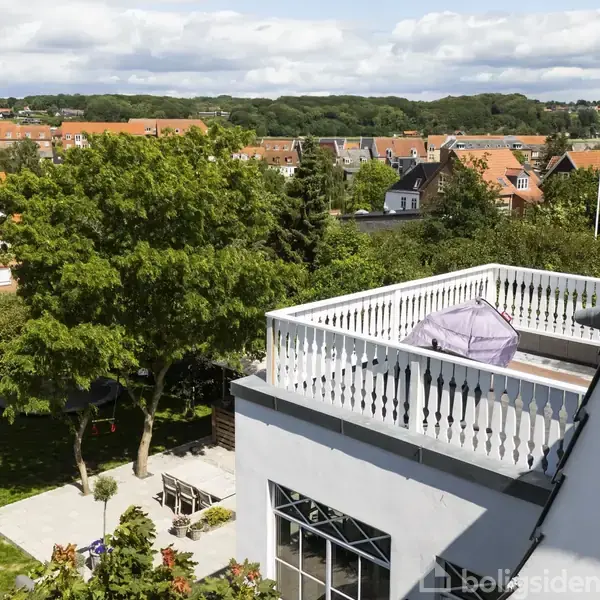 Takterrasse med grill dækket af et cover står stille på en bygning. Omgivet af grønne træer og haver med udsigt til rødtagsklædte huse i et villakvarter.
