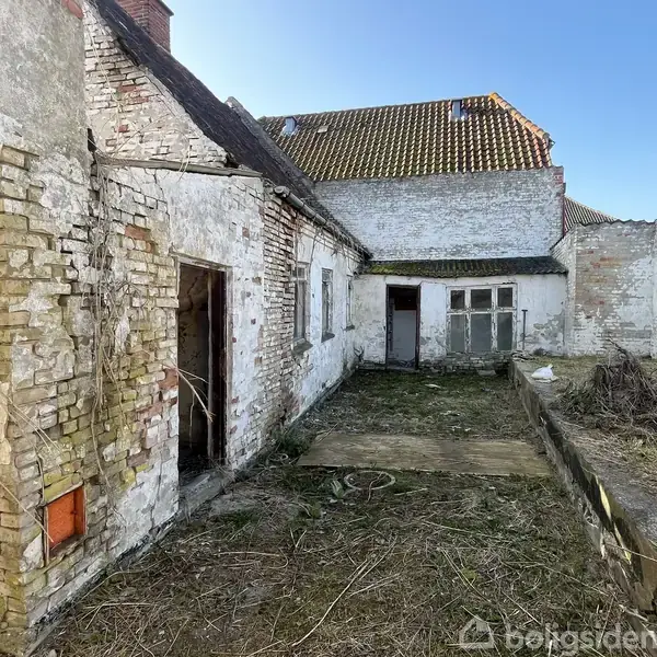 Forladt hus i forfald med mursten og delvist kollapset tag. Detaljer omfatter åbne døre og et overgroet gårdområde omgivet af slidte vægge.