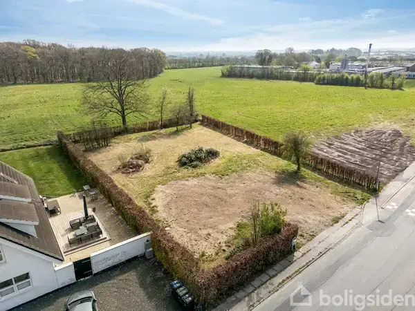 Grunden er en rektangulær have omkranset af hække, med et par buske i midten. Den ligger ved siden af et hus og en landevej, omgivet af marker.