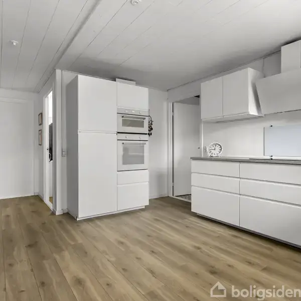 Et moderne køkken med hvide skabe og apparater som ovn og emhætte. Rummet har et lyst plankegulv og en lysdækket væg med en dør i baggrunden.