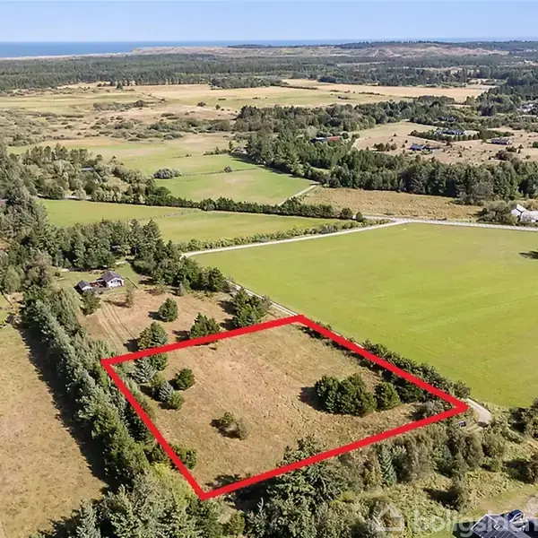 Et kvadratisk markareal indrammet med røde linjer ligger blandt grønne åbne marker og små skovområder. Omkringliggende skov og bebyggelse kan ses i baggrunden.