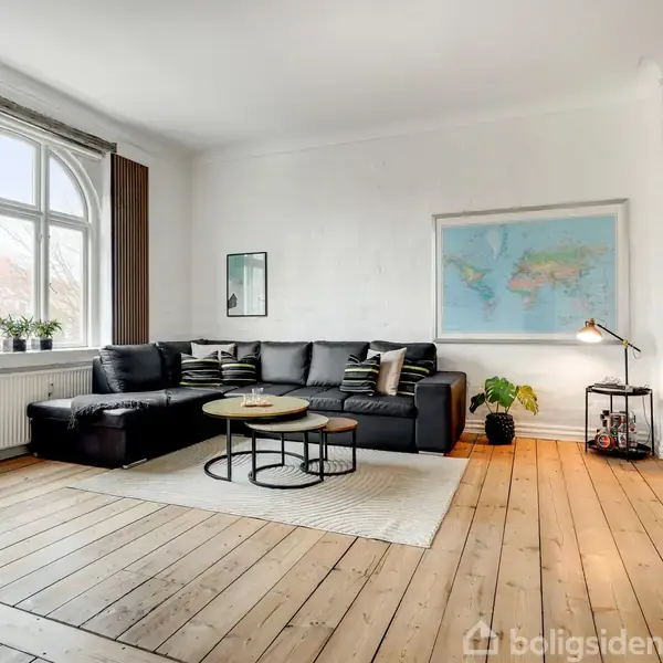 Sort hjørnesofa står på et lyst træparketgulv. Sofaen er omgivet af et sofabord, en gulvlampe og en tv-enhed. Væggen har et verdenskort og et vindue med udsigt.