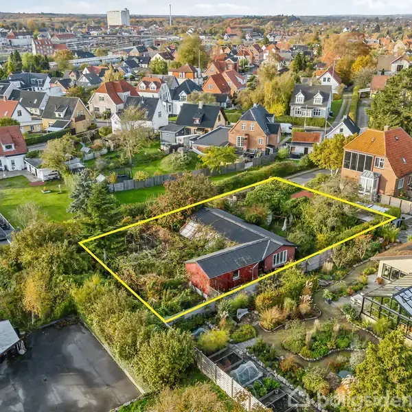 Et rødt hus er omgivet af en stor have markeret med en gul linje i et beboelsesområde med mange huse. Haver og træer omringer bygningen.