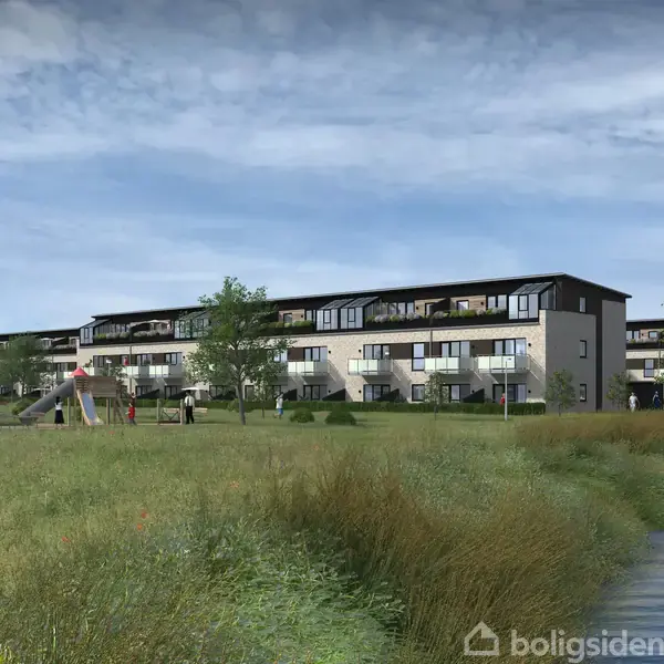 Flere rækkehuse står langs en grøn plads, hvor mennesker går og børn leger på en legeplads. Området er omgivet af træer og kan ses nær en sø.