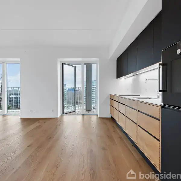 Køkken med sorte skabe og integreret ovn, der står i skarp kontrast til lyse træpaneler. Store vinduer åbner mod en balkon med udsigt over byen.