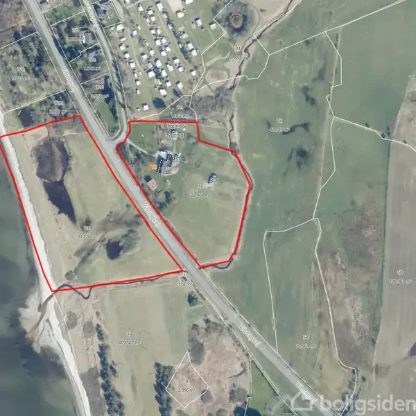 Luftfoto viser to indhegnede landområder tæt ved en kystlinje. Et vejnet og spredte bygninger ses omkring områdegrænserne. Vand er på venstre side, omgivet af marker og skove.