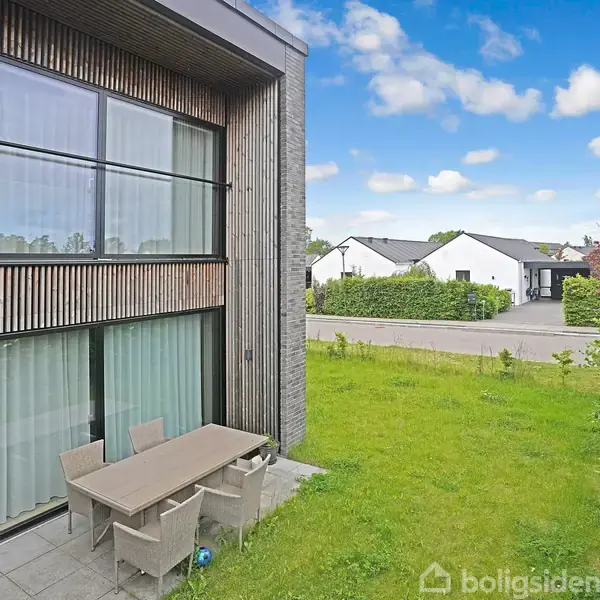 Et moderne køkken har en hvid køkkenø med planter. Køkkenet har hvide skabe, en ovn og en kedel til venstre. Væggene er grønne, og en glasvitrine står ved siden af en dør.