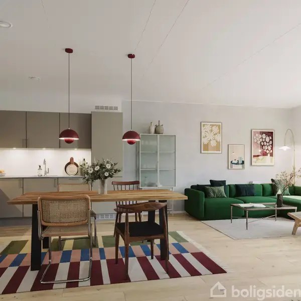 Et moderne køkkenalrum med spisebord og stole i forgrunden. Et grønt sofaområde med billeder på væggen udgør baggrunden. To hængelamper lyser rummet op.