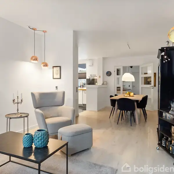 Stue med moderne indretning; gråt lænestolssæt foran et sofabord med blå dekorationer. Sort reol med globus, ved spisebord under pendellampe. Vægkunst: "Marilyn Monroe" i sort/hvid.