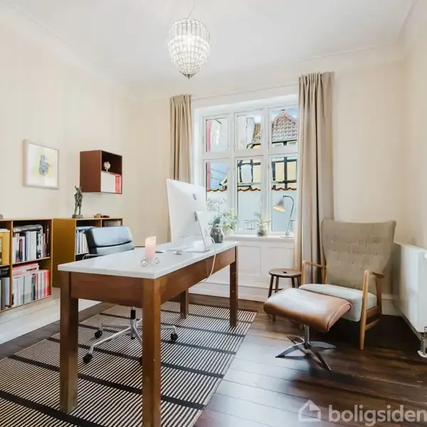 Et lyst kontor med et skrivebord i midten, omgivet af moderne møbler og dekorationer. Vinduer lukker naturligt lys ind, mens reoler med bøger fylder baggrunden.