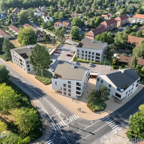 En gruppe moderne lejlighedsbygninger står stille blandt frodige træer. Omkring dem løber veje med fodgængerovergange, omgivet af en bymæssig, grøn forstad med flere hustage og træer.
