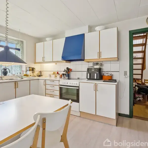 Et køkken med hvide skabe udfører madlavningsfunktion, omgivet af en ovn, mikrobølgeovn og diverse køkkenredskaber. På væggen står "Everyday love", køkkenbordet er centralt placeret.