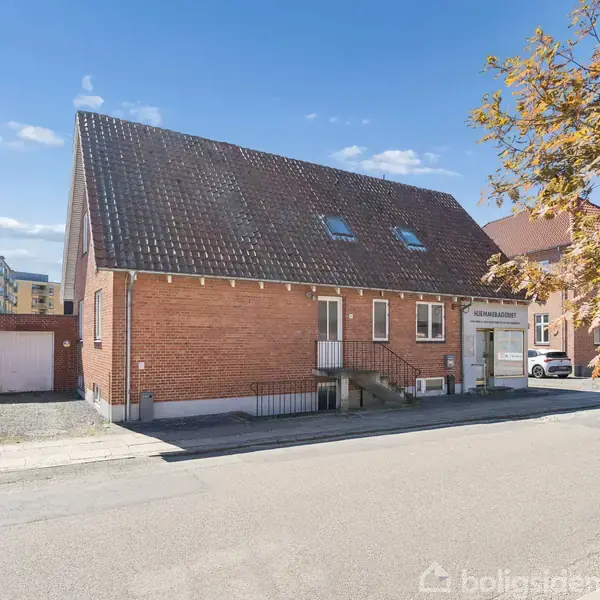 En etagebygning i røde mursten med skråt tag, står i et byområde. Der er træer langs fortovet. Tekst på bygning: "Åbyhøj Dyreklinik".