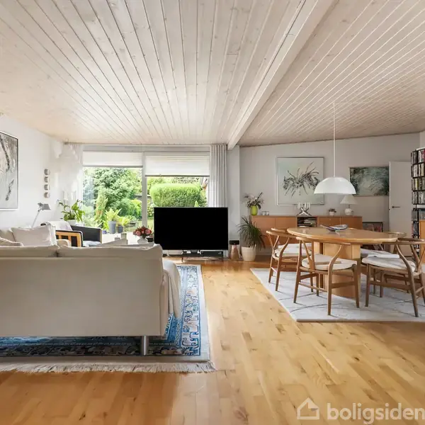 Stue med hvid sofa, rektangulært sofabord og fladskærms-TV. Spiseområde inkluderer træbord og stole under hængelampe. Store vinduer slipper lys ind; grøn udsigt udenfor. Trægulv og loft i lyst træ.