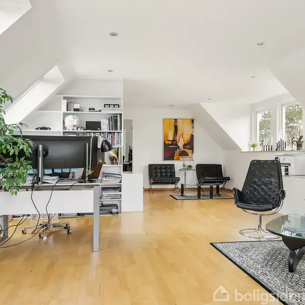 Et moderne kontor- og dagligstueområde med bærbare computere på skrivebordet, omgivet af hvide vægge og møbler. Stueplan indeholder et lille tæppe og glasbord, med vinduer langs væggen.