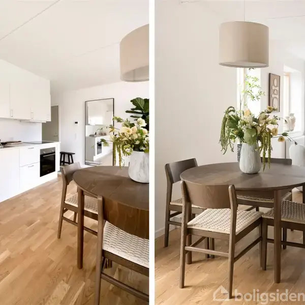 Et rundt træbord med stole står i et lyst køkken-alrum. Bordet er dekoreret med en vase med blomster og en lampe over. I baggrunden ses et moderne køkken og en stue.