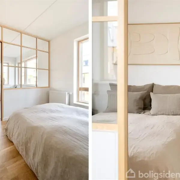 Soveværelse med dobbeltseng dækket af beige sengetøj. Glasvægge adskiller rummet fra et tilstødende kontor med skrivebord og stol. Trægulve og minimalistisk kunst på væggen.