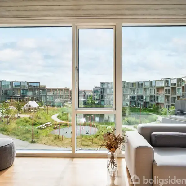 Sofa står i en moderne stue ved store vinduer. Udenfor ses en grøn have med en stiforbindelse og omkringliggende lejlighedsbygninger.