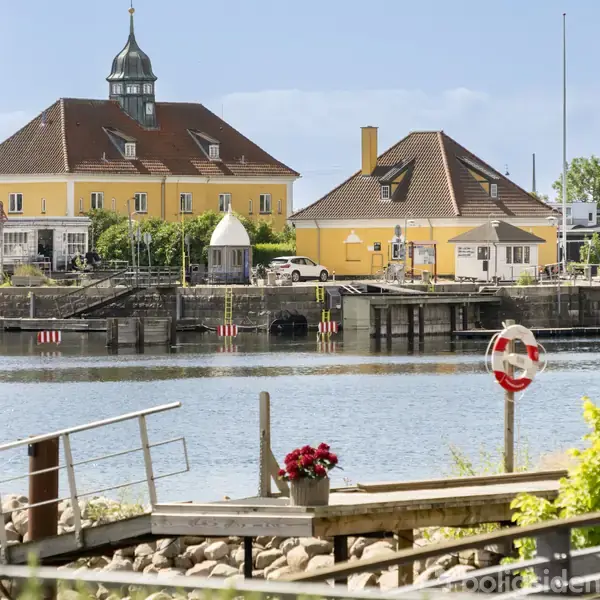 Stue med moderne indretning, der har store vinduer, som slipper masser af lys ind. Køkkenet er til venstre, mens en rund stol og et bord står til højre. Udsigt til bylandskab.
