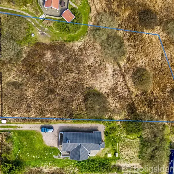 Grunden er markeret med en blå linje i et luftfotografi. En bil er parkeret ved et hus med en mørk tag. Vejen løber langs venstre side.