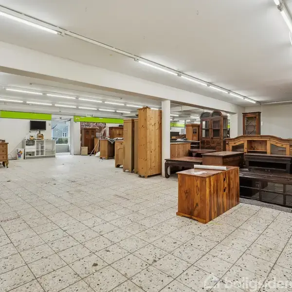 Butikker møbler står opstillet i et stort rum med hvide vægge og loftsbelysning. Flisegulvet strækker sig ud i lokalet, hvor væggen bærer skiltet "ØKO LANDET".