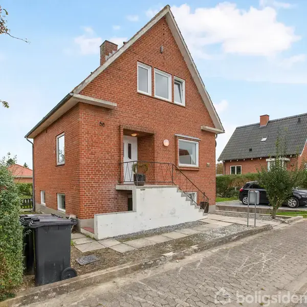 Et rødt murstenshus står ved en stille villavej. Trappen fører op til hoveddøren, og en skraldespand står ved siden af. Biler er parkeret tæt på i indkørslen.