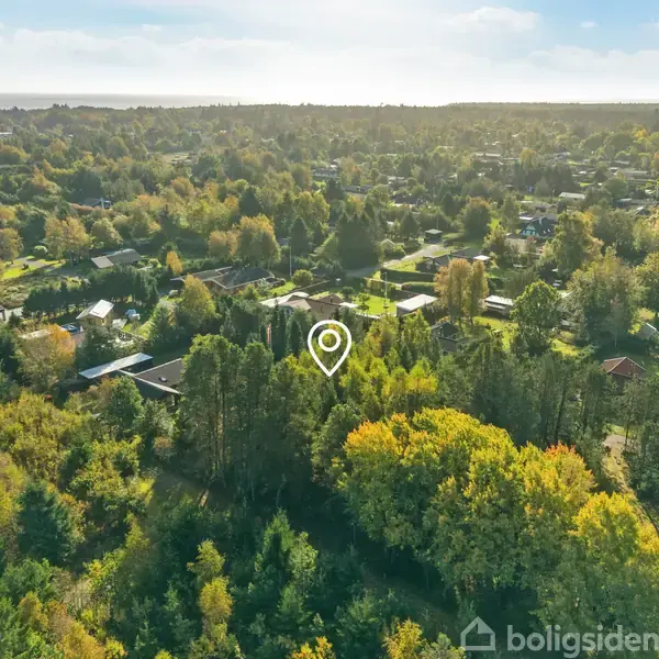 Et hus ses fra luften, markeret med en hvid pin. Det er omgivet af frodig skov og mindre boliger i en landlig område.
