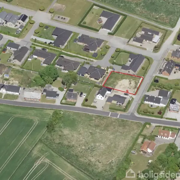 Boligområde med rækkehuse og grønne marker omkring. En ubebygget grund markeret med rød streg i centrum. Veje og beboelse omringer grunden i et fredeligt kvarter.