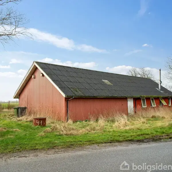 Et rødt hus med sort tag står i et græsbevokset område ved en vej. Omkringliggende træer og buske giver en landlig atmosfære. På skiltet står der "41".