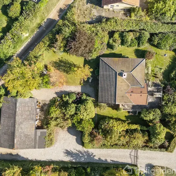Huse fra oven omringet af grønne haver og træer. Der er to bygninger med grusveje, der forbinder dem. Området er frodigt og velplejet.