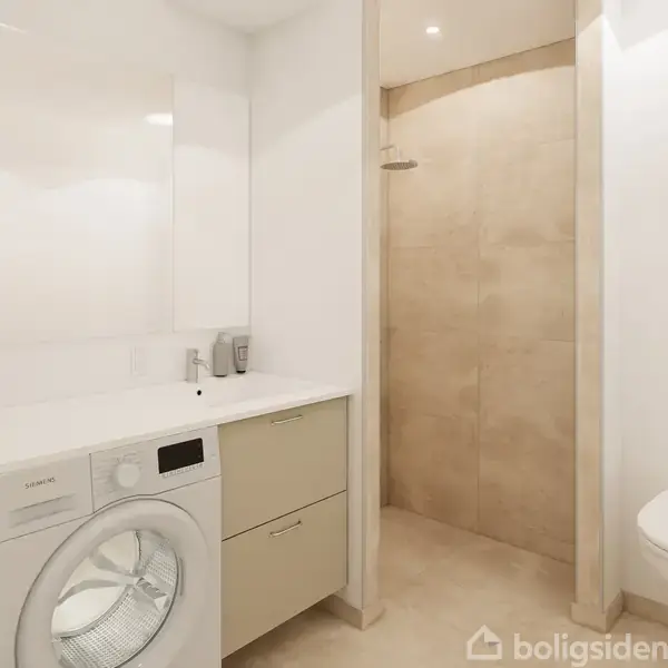 Vaskemaskine og tørretumbler står under en hvid bordplade med skabe ovenover. Et badeværelse med hvidt og beige interiør inkluderer en toilet og brusekabine i baggrunden.