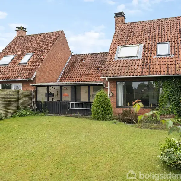 Rødt murstenshus med tagvinduer står stille i en grøn have. En træhegn danner grænse mellem græsplænen og de røde mursten.