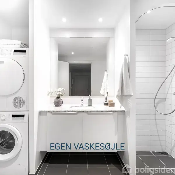 Vaskesøjle med vaskemaskine og tørretumbler ved siden af et moderne badeværelse. En hvid vask med spejl og bruser i glasafskærmning. Tekst: "EGEN VASKESØJLE".
