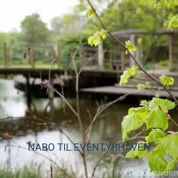 Bro strækker sig over en lille sø med frodig, grøn bevoksning i nærheden. Tekst: "NABO TIL EVENTYRHAVEN." Det er en rolig og naturskøn scene.