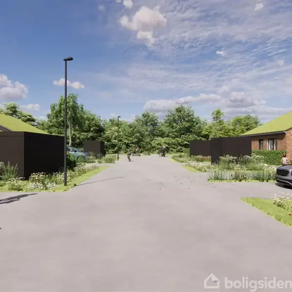 Gade med asfaltvej omgivet af moderne huse, nogle med grønne tage. En person går på fortovet, og biler er parkeret. Grønne planter præger omgivelserne, under en blå himmel med skyer.