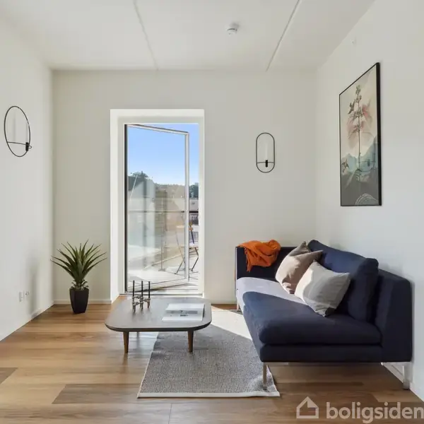 En stue med en blå sofa, placeret ved siden af et lille sofabord og en potteplante, med en åben dør mod en solrig altan. Vægdekoration inkluderer en plakat.