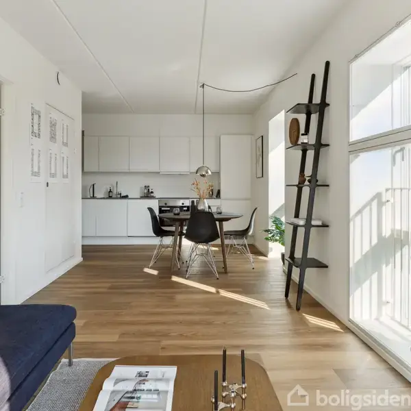 En moderne stue med en blå sofa til venstre. Et spisebord med fire stole er placeret i midten. Rummet er lyst op af store vinduer og en stigehylde står til højre.