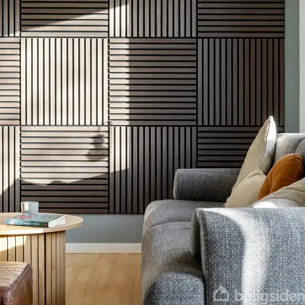 En grå sofa med puder står i en moderne stue. En rund træbord har en bog og et krus. Mørke træpaneler dækker væggen.