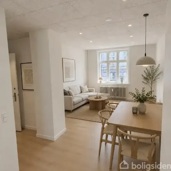 Sofaen står i en lys stue med et sofabord foran og et stort vindue i baggrunden. Ved siden af er et spisebord med stole og en lampe hænger over bordet.