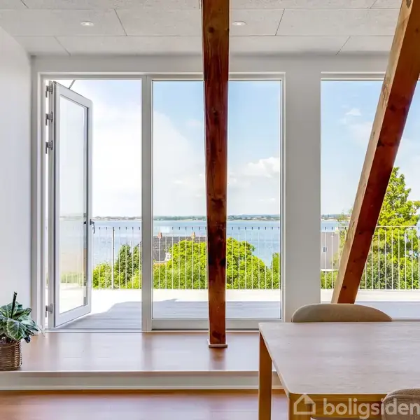 Et byområde ligger langs en kystlinje med huse og grønne områder. Der ses et markeret punkt med teksten "REAL" over en bygning, omgivet af flere bygninger og landskab.
