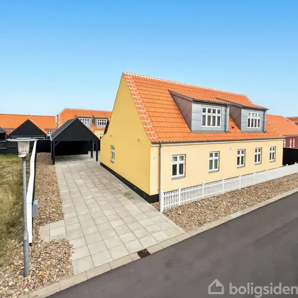 Et gult, to-etagers hus med rødt tegltag står på en brolagt indkørsel. Ved siden af er en carport. Omkringliggende huse og en vej danner boligområdet.